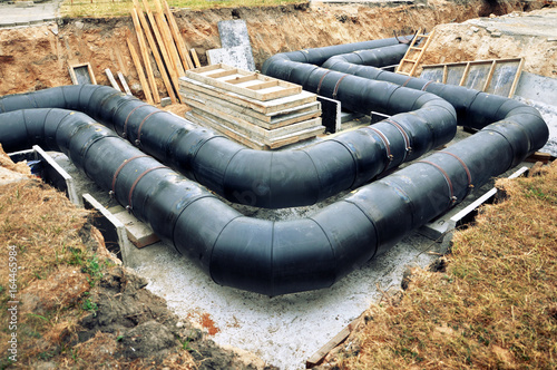 The process of laying of engineering heating systems. Two turning black plastic pipes in sandy trench.