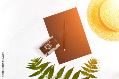 Straw hat with green leaves and old camera on white background, Summer background. Top view. Sun flare photo