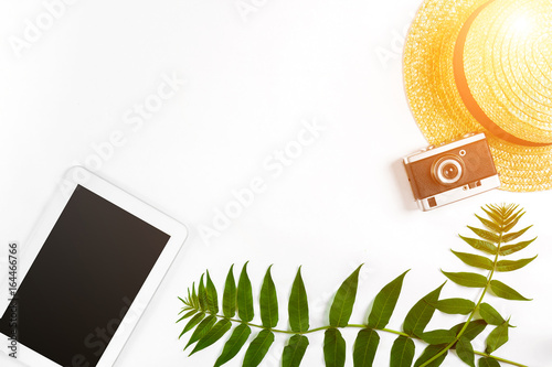 Straw hat with green leaves, tablet and old camera on white background, Summer background. Top view. Sun flare photo