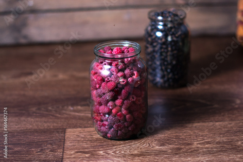 Fresh raspberry berries in a glass jar on a wooden background.