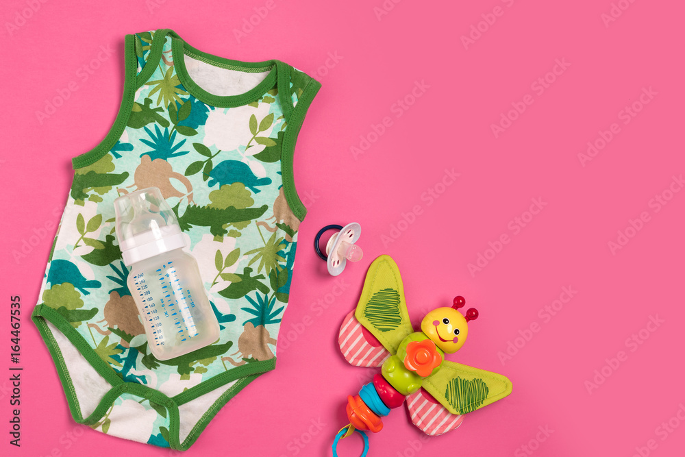 White and green bodysuit and bottle on pink background. Things for babies. Top view.