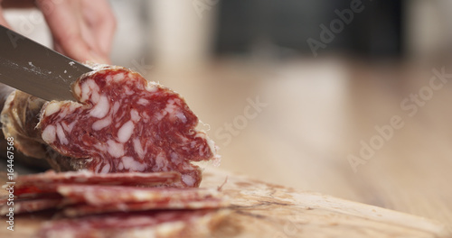 female teen hand slicing dried italian salami