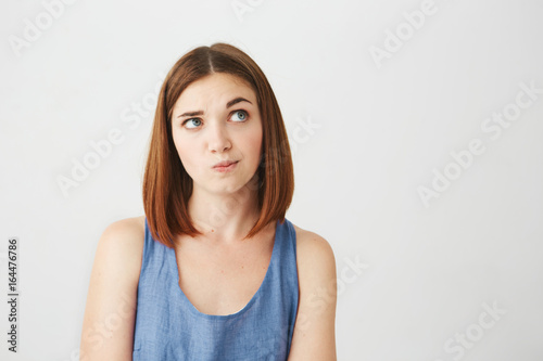 Young beautiful girl looking up thinking raising brow over white background.