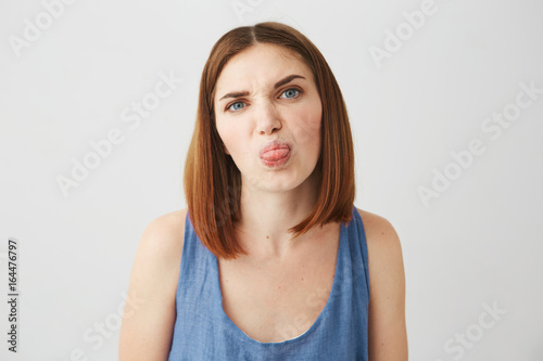 Cheerful young pretty brunette girl showing tongue making funny face looking at camera over white background.