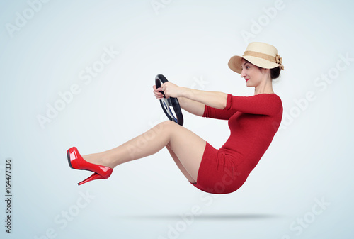 Young woman in red dress and hat drives a car with steering wheel