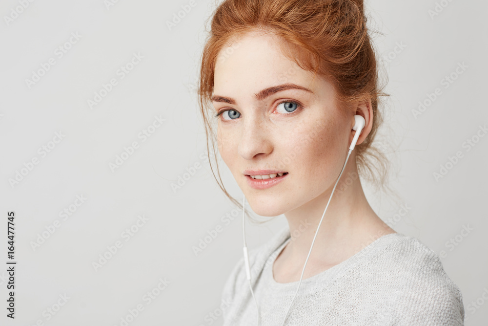 Portrait of young beautiful tender redhead girl with blue eyes in headphones looking at camera smiling over white background. Portrait of young beautiful tender redhead girl with blue eyes in headphones looking at camera smiling over white background.