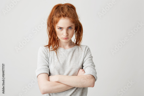 Картината върху платно Portrait of resentful young pretty redhead girl looking at camera brutally with crossed arms over white background
