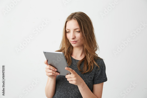 Young pretty girl smiling looking at tablet surfing web browsing internet over white background.