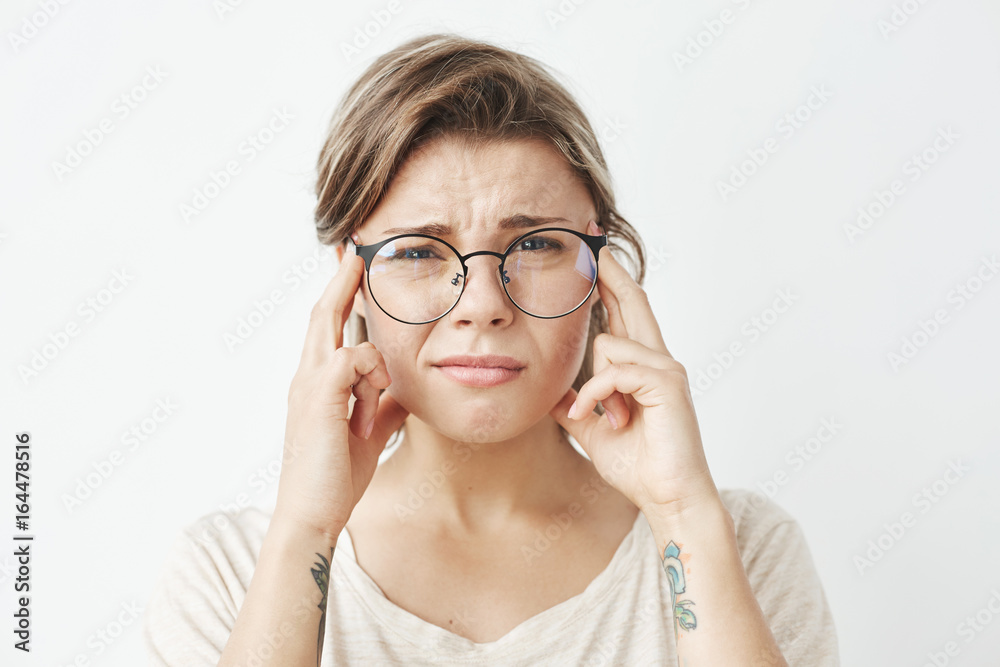 Young pretty girl in glasses thinking frowning looking at camera with fingers on temples over white background. Young pretty girl in glasses thinking frowning looking at camera with fingers on temples over white background.