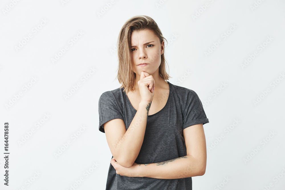 Young beautiful girl thinking with hand on chin looking at camera frowning over white background. Young beautiful girl thinking with hand on chin looking at camera frowning over white background.