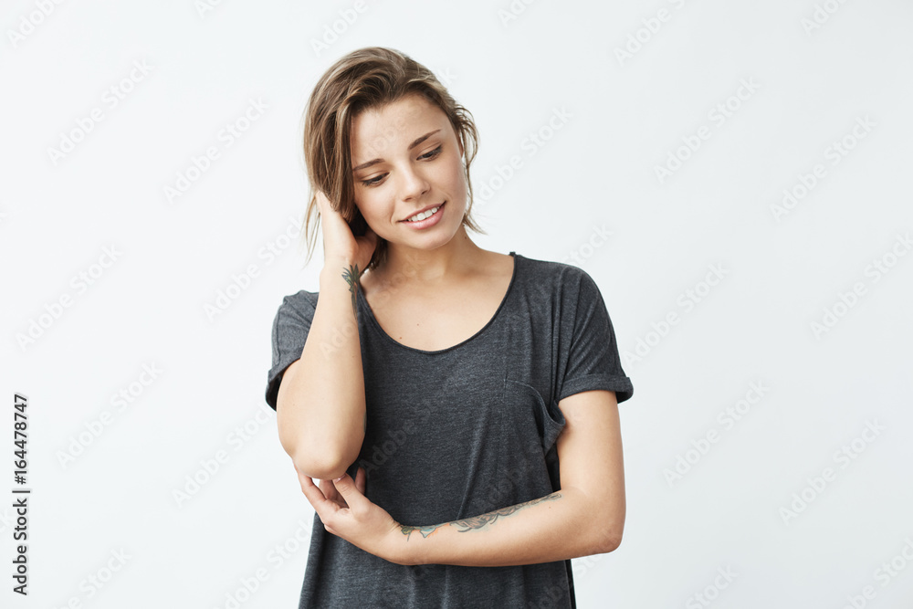 Shy young pretty tattooed girl smiling looking down over white background. Shy young pretty tattooed girl smiling looking down over white background.