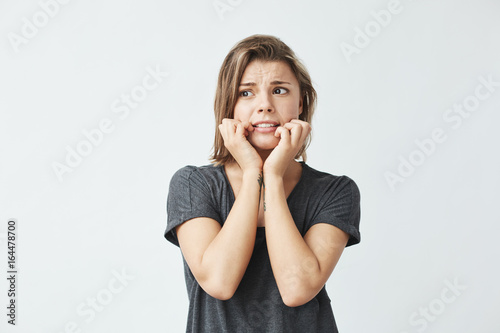 Nervous young beautiful girl holding hands on cheeks over white background.