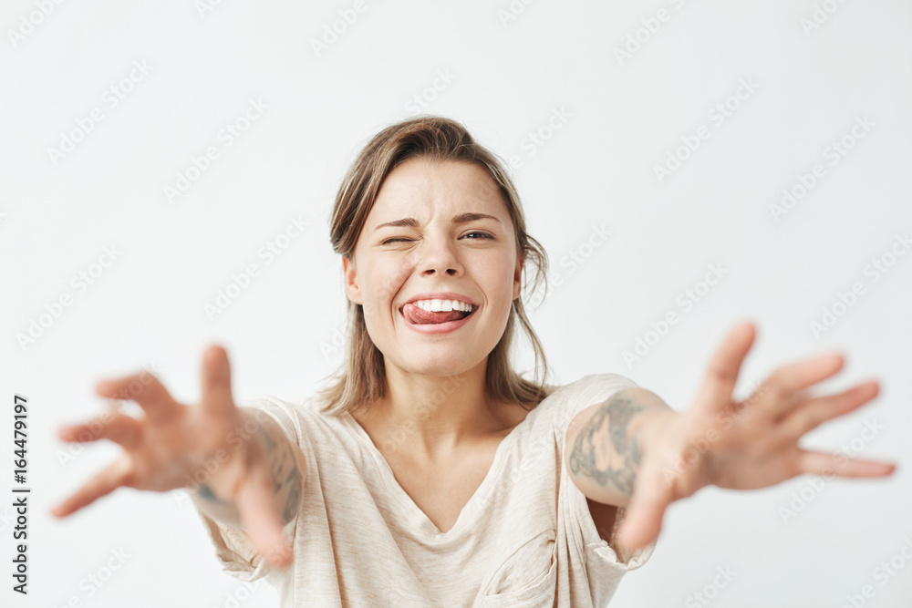 Young funny pretty girl winking showing tongue stretching hands to camera over white background. Young funny pretty girl winking showing tongue stretching hands to camera over white background.