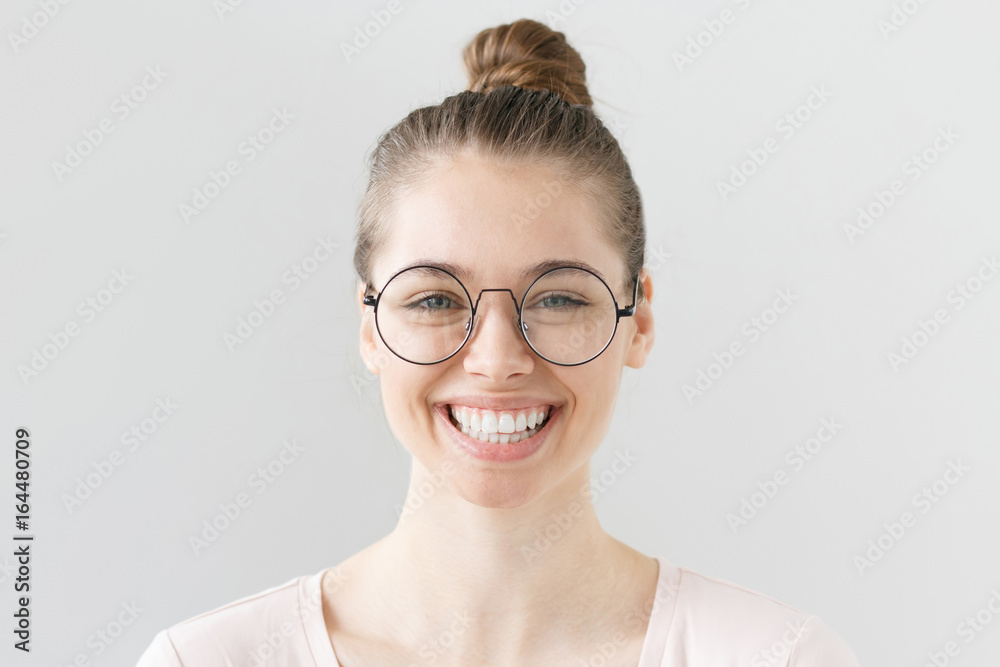 Indoor portrait of young beautiful woman isolated on gray background,  smiling, blinking behind big round glasses with expression of full content,  satisfaction and happiness with current situation. Stock Photo | Adobe Stock