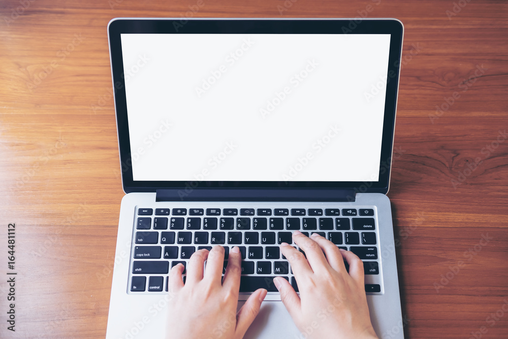 Mockup image of hand using and typing on laptop with blank white screen on wooden table in office Mockup image of hand using and typing on laptop with blank white screen on wooden table in office