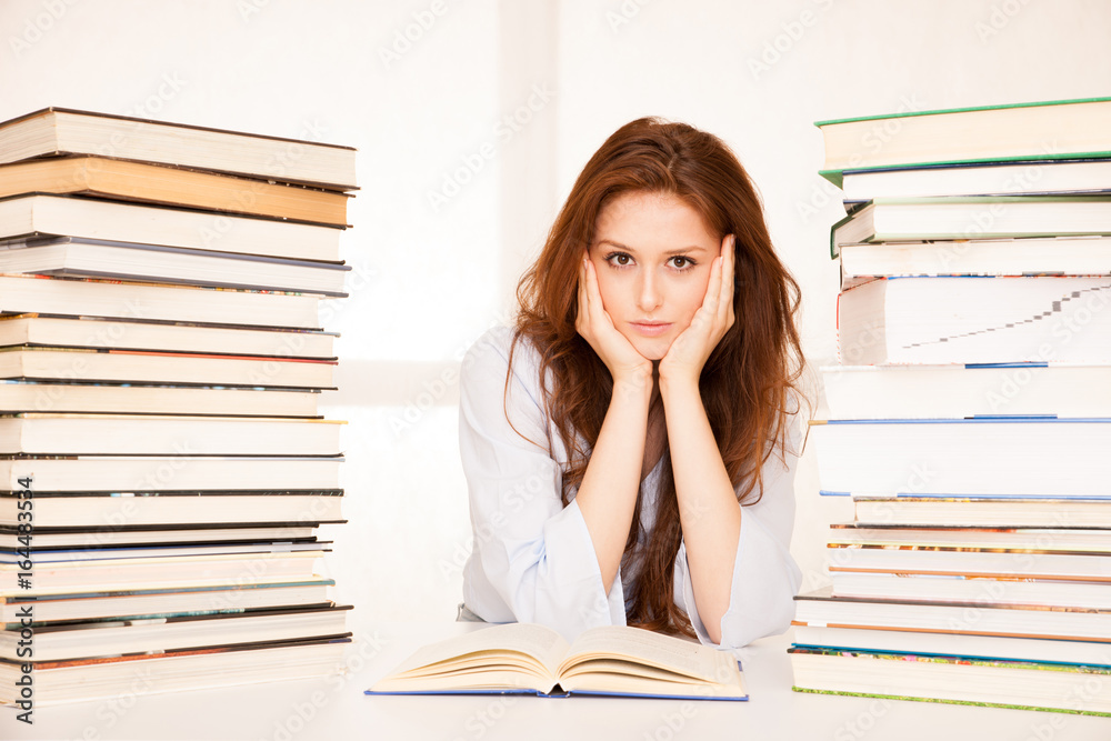 attractive young woman studies wtih hugr book piles on her desk attractive young woman studies wtih hugr book piles on her desk