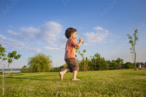 child with a bottle running along the grass. © zhukovvvlad