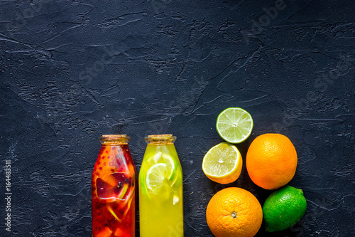 Bottle of fresh lemonade and fruits on black stone background top view copyspace