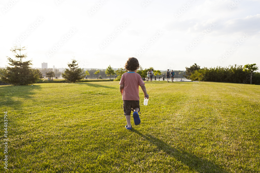 child with a bottle running along the grass.