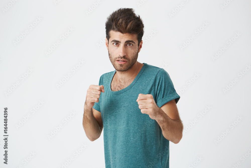 Strong, resolute man in blue t-shirt with beard standing in a fighting stance on a white background. Male student getting ready to defend his honour. Strong, resolute man in blue t-shirt with beard standing in a fighting stance on a white background. Male student getting ready to defend his honour.