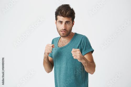 Strong, resolute man in blue t-shirt with beard standing in a fighting stance on a white background. Male student getting ready to defend his honour. photo