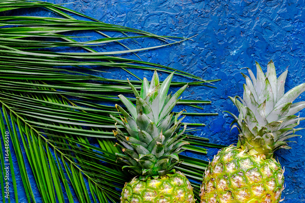 Fototapeta Pineapple and palm branch on blue table background top view