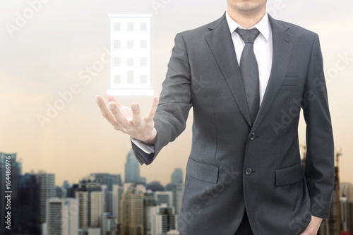 Double exposure of young handsome confident professional businessman holding condominimium illustation and night cityscape with modern office building background, Business & Real estate agency concept