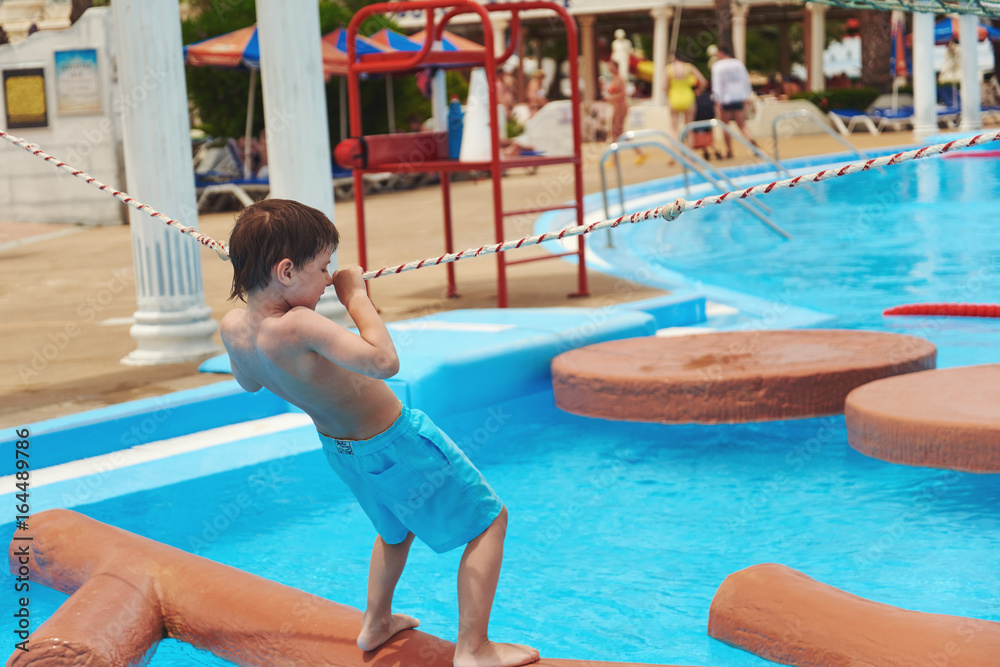 Boy crossing waterpark fake river with rope.