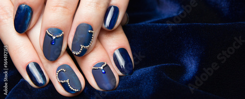 Fotografia French manicure - beautiful manicured female hands with blue manicure with rhinestones on dark blue background, border design panoramic banner