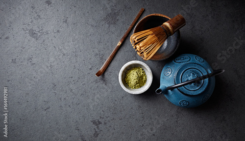 An arrangement of a cast iron tea pot, matcha powder and tea whisk