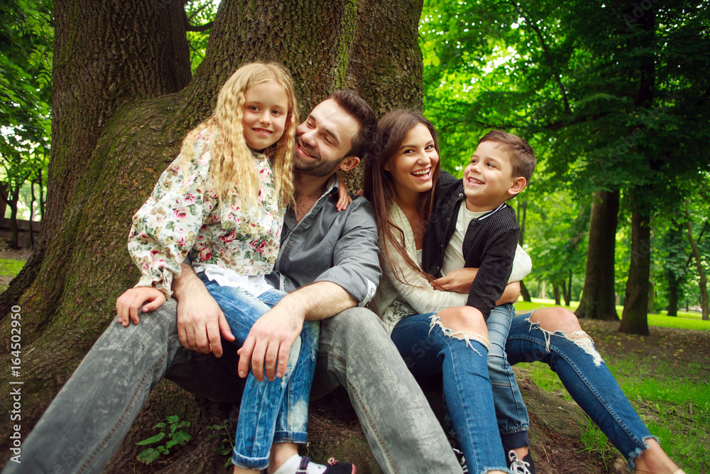 Happy family sitting together at tree in summer forest