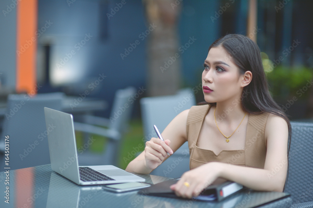 Sharing good business news. Attractive young woman talking on the mobile phone and smiling while sitting at her working place in office and looking at laptop, businesswoman working. Selective focus. Sharing good business news. Attractive young woman talking on the mobile phone and smiling while sitting at her working place in office and looking at laptop, businesswoman working. Selective focus.