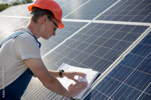 Employee working with drawings on solar energy station. Worker looking in technical documants on solar panel. photo