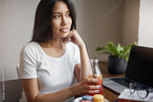 Young asian female drinking lemonade in cafe using laptop.
