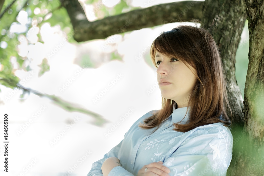 A woman leaning against a big tree alone in the park A woman leaning against a big tree alone in the park