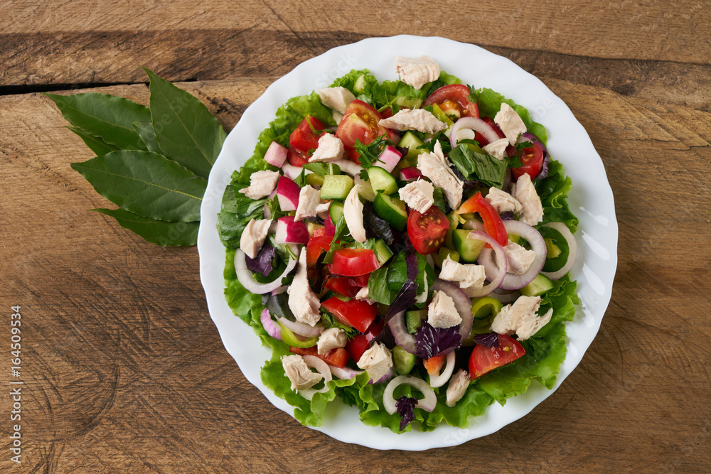 Top view of a fresh salad with smoked chicken meat and fresh vegetables: cucumber, bell pepper, garlic, onion and cherry tomatoes on old wooden table. Delicious dinner table. Healthy eating.