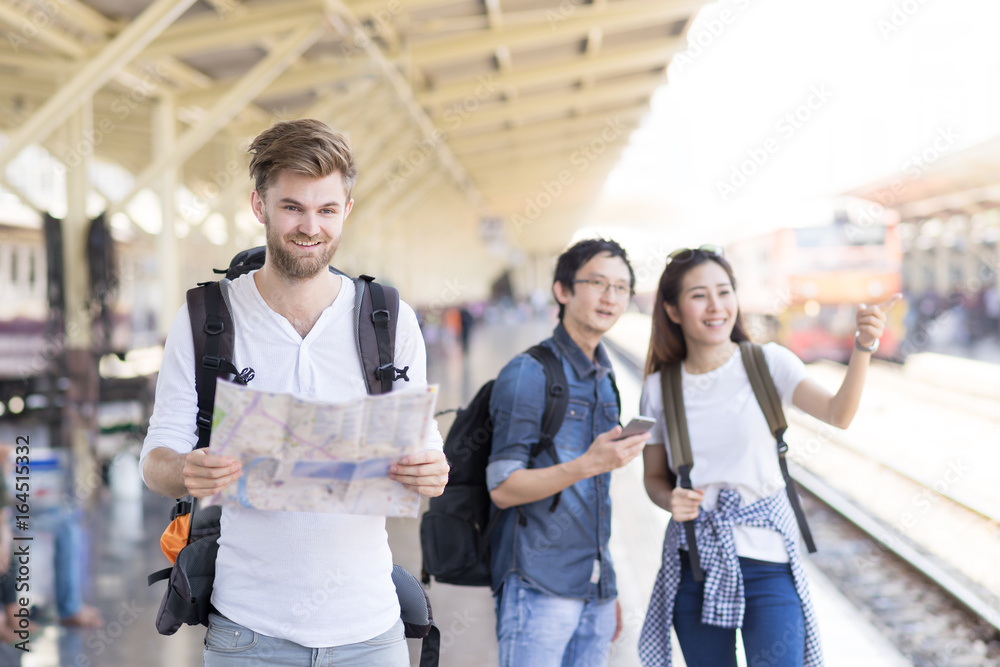 Multi ethnic group of friend backpack traveler using local map and smartphone for navigation at train station, Asian tourism travel in summer holiday concept.