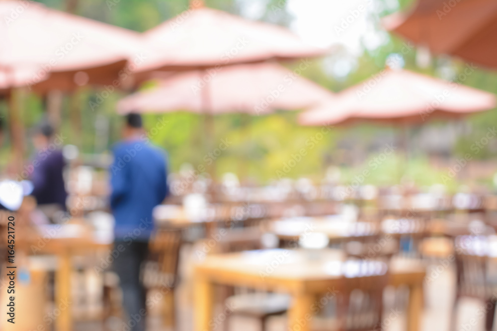 Blurred image as background of outdoor restaurant with tables, chairs & parasols