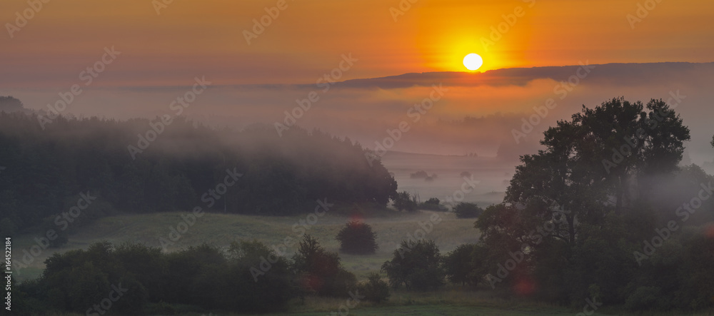 Foggy summer morning over the valley, fog and rising sun