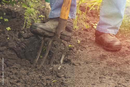 fragment of men's leg digging soil with pitchfork close up view