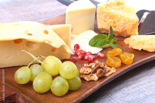 Assortment of cheese with fruits  grapes  nuts and cheese knife on a wooden serving tray.