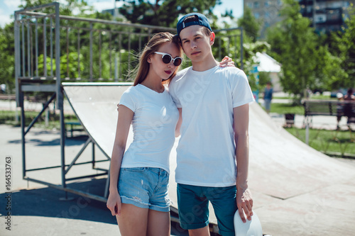 Young couple in white T-shirts posing in skate park. Mock up.