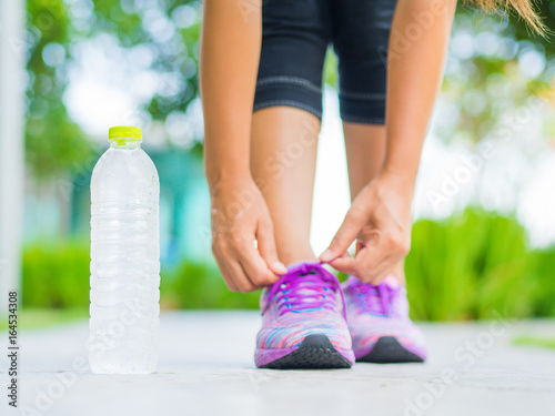 Running shoes - closeup of woman tying shoe laces. Female sport fitness runner getting ready for jogging with water bottle in garden backgroound