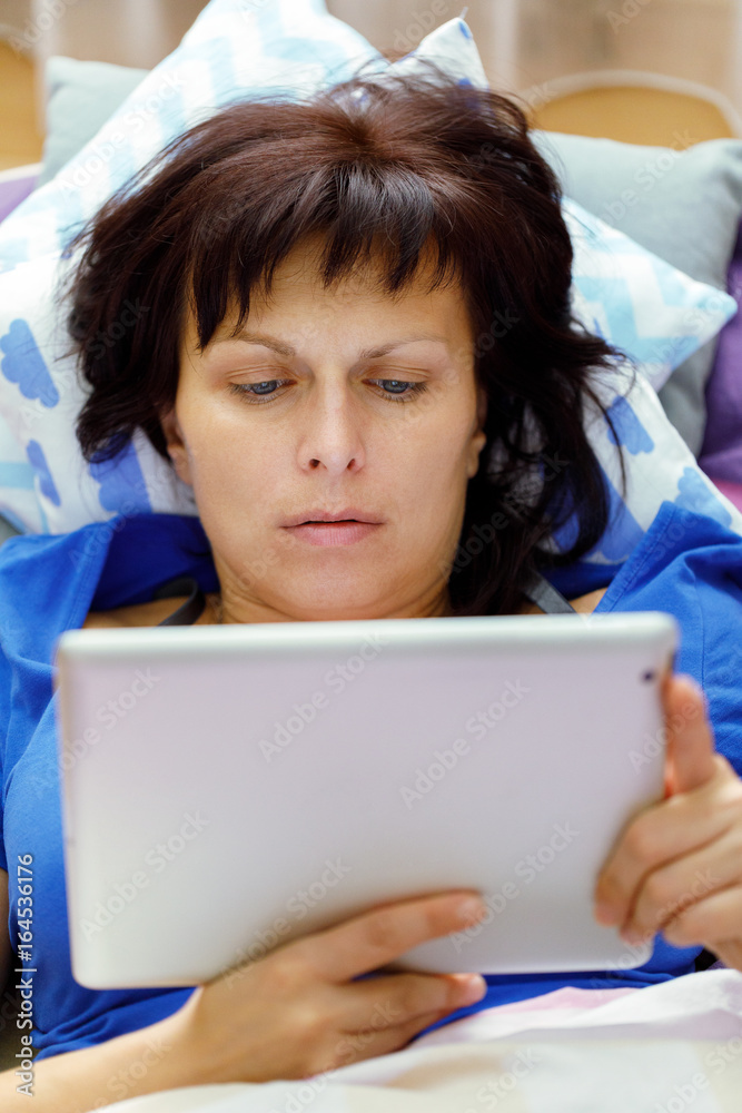 Middle age woman resting in bed with tablet Middle age woman resting in bed with tablet
