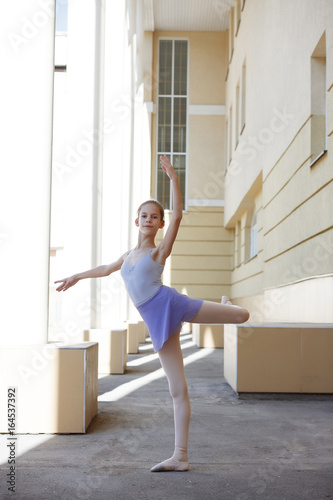 Ballet dancer dancing on street. Young ballerina on yellow background full length