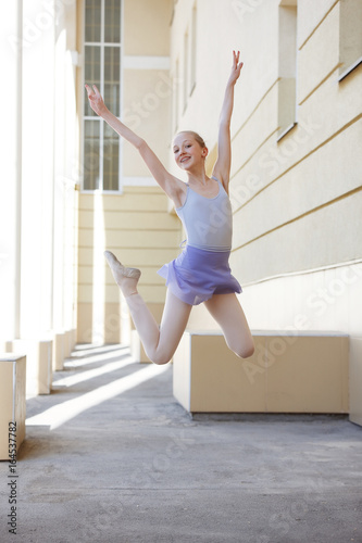 Ballet dancer dancing on street. Young ballerina on yellow background full length