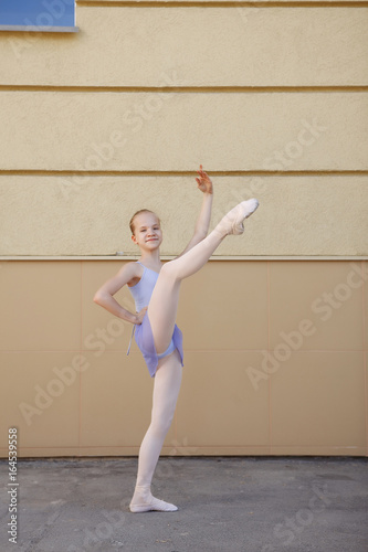 Ballet dancer dancing on street. Young ballerina on yellow background full length