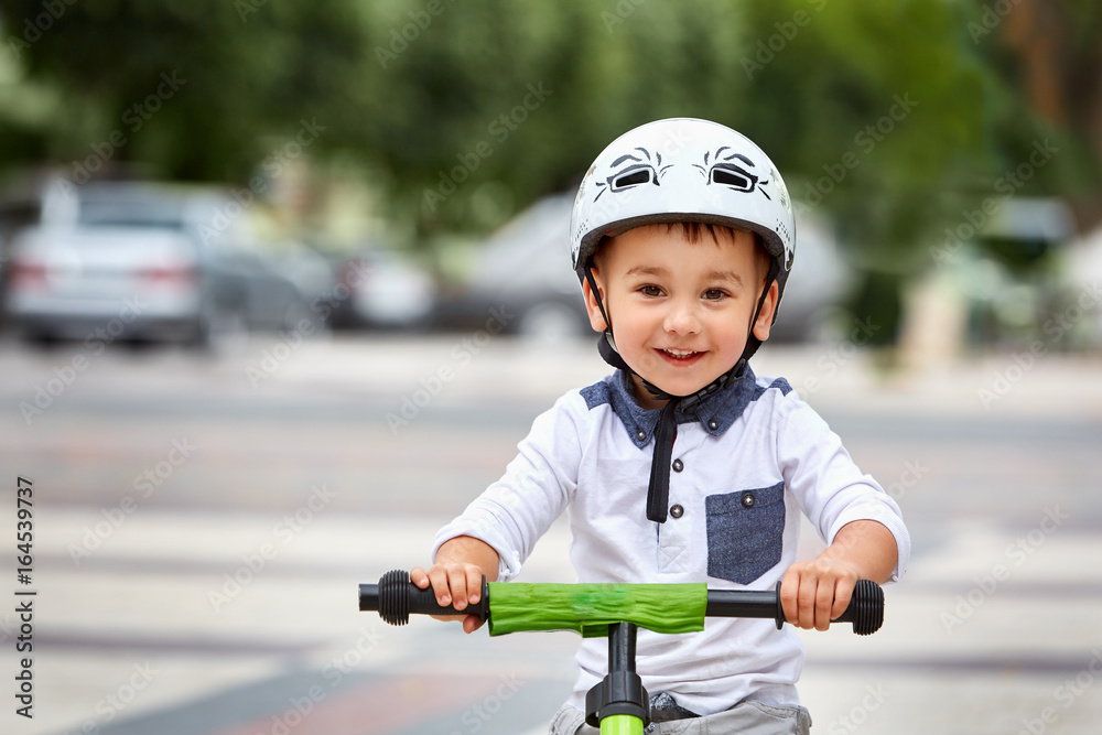Obraz premium Little boy kid in helmet ride a bike in city park. Cheerful child outdoor.