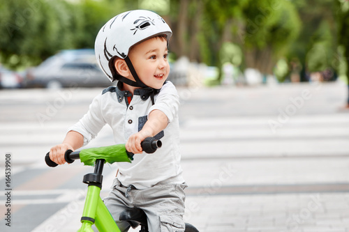 Little boy kid in helmet ride a bike in city park. Cheerful child outdoor.