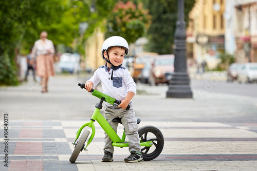 Little boy kid in helmet ride a bike in city park. Cheerful child outdoor. © Aleksey